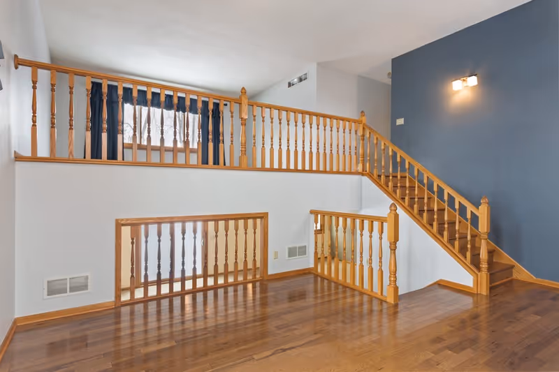 Two-story interior with wood railings, polished hardwood floor, and blue accent wall.