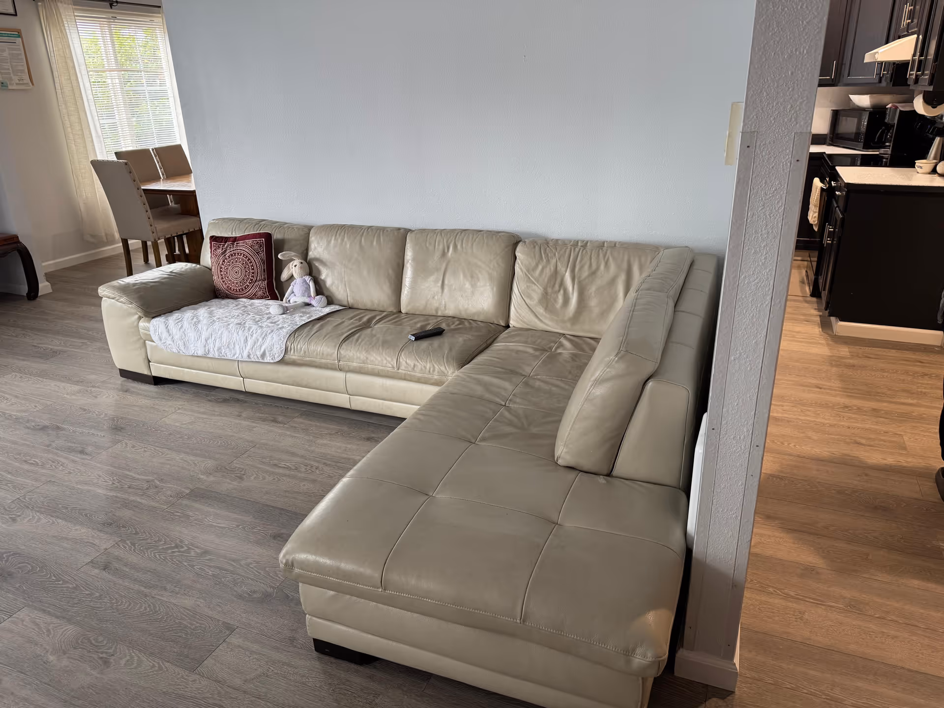 Beige leather sectional sofa in a living room with a stuffed toy and remote.