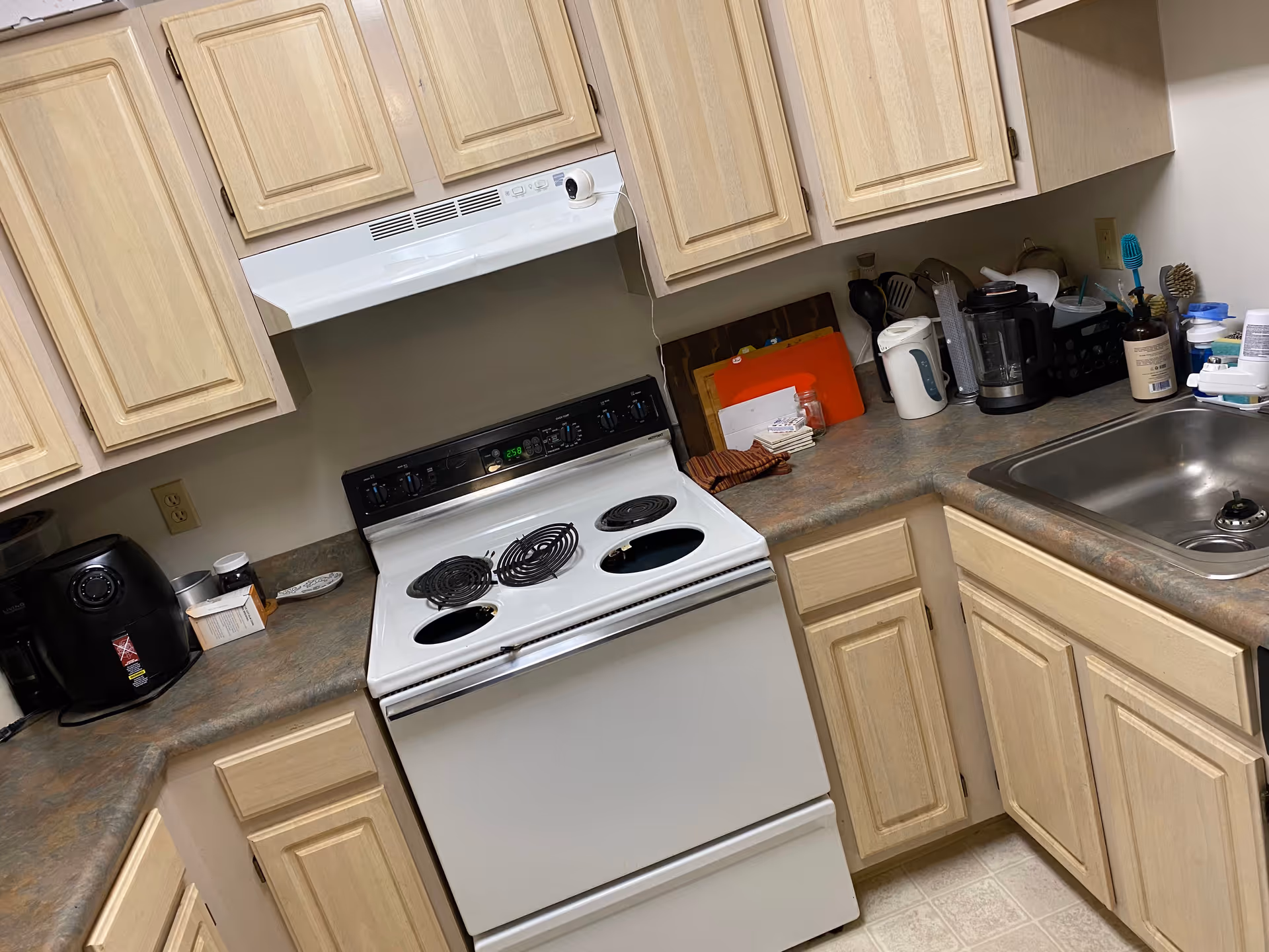Small kitchen with beige cabinets, electric stove, sink, and appliances on the counter.