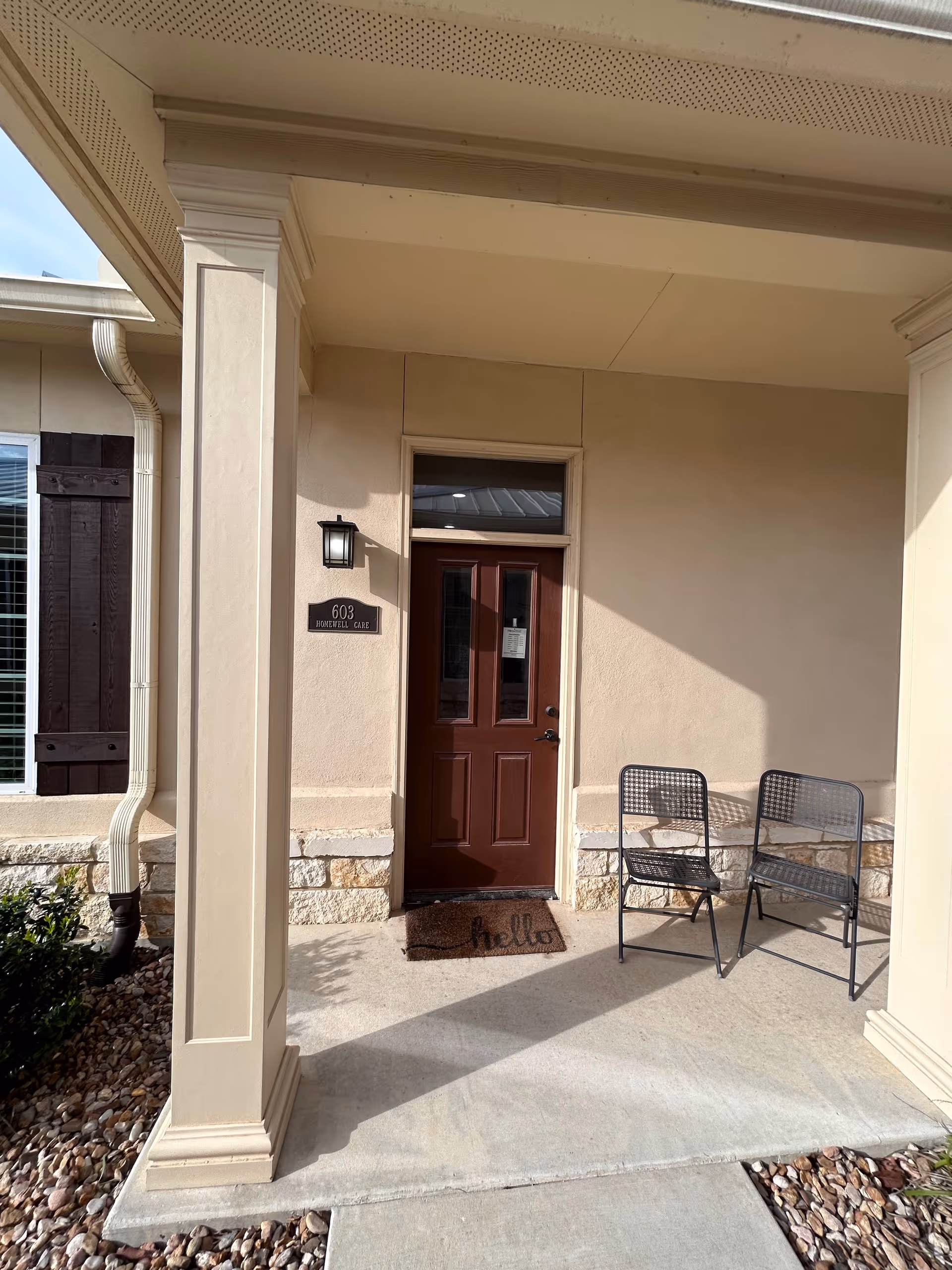 Exterior entryway of a HomeWell Care Services building with a welcome mat and two metal chairs.