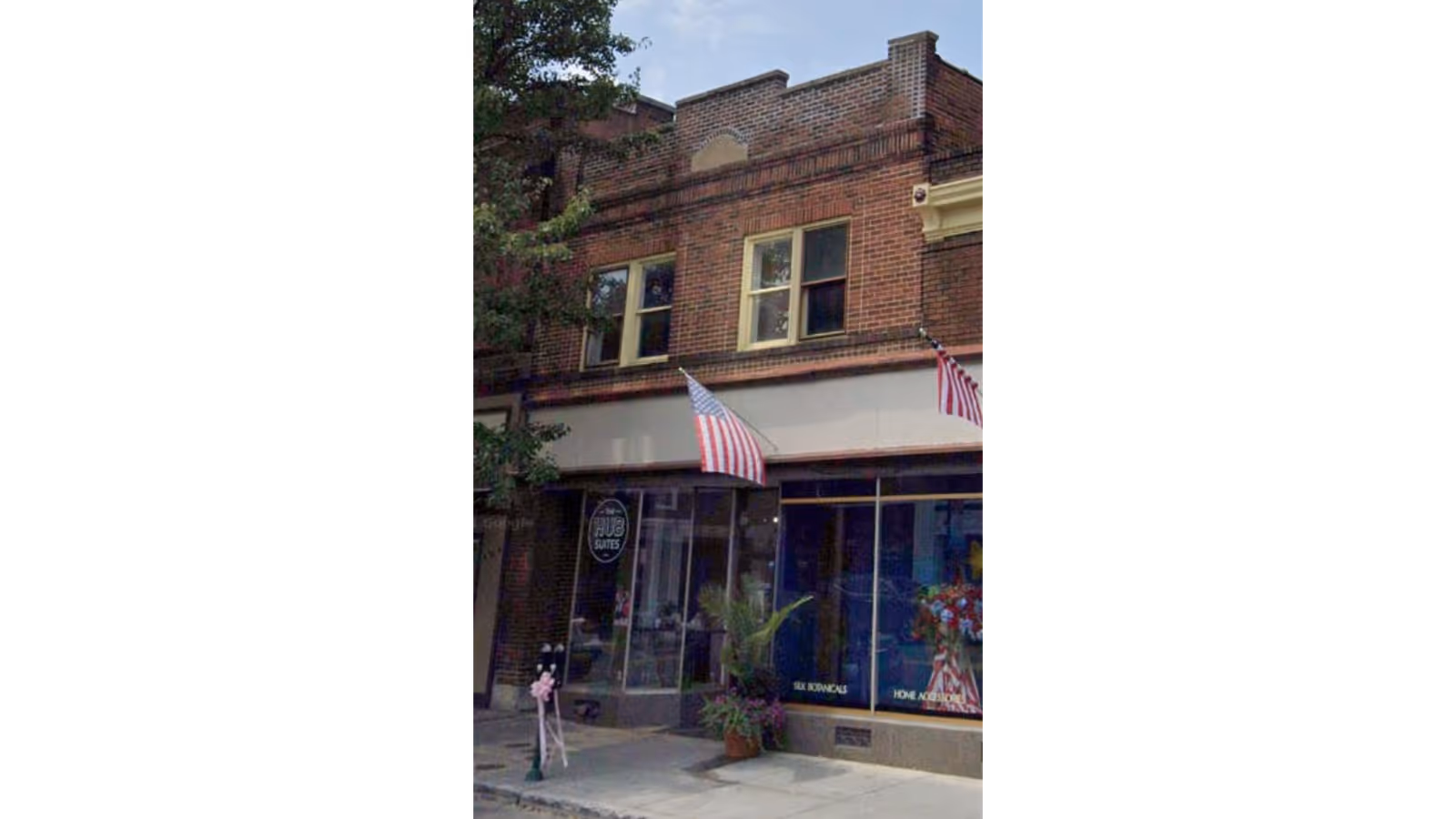 Brick storefront of Village Caregiving with flags and potted plants outside.