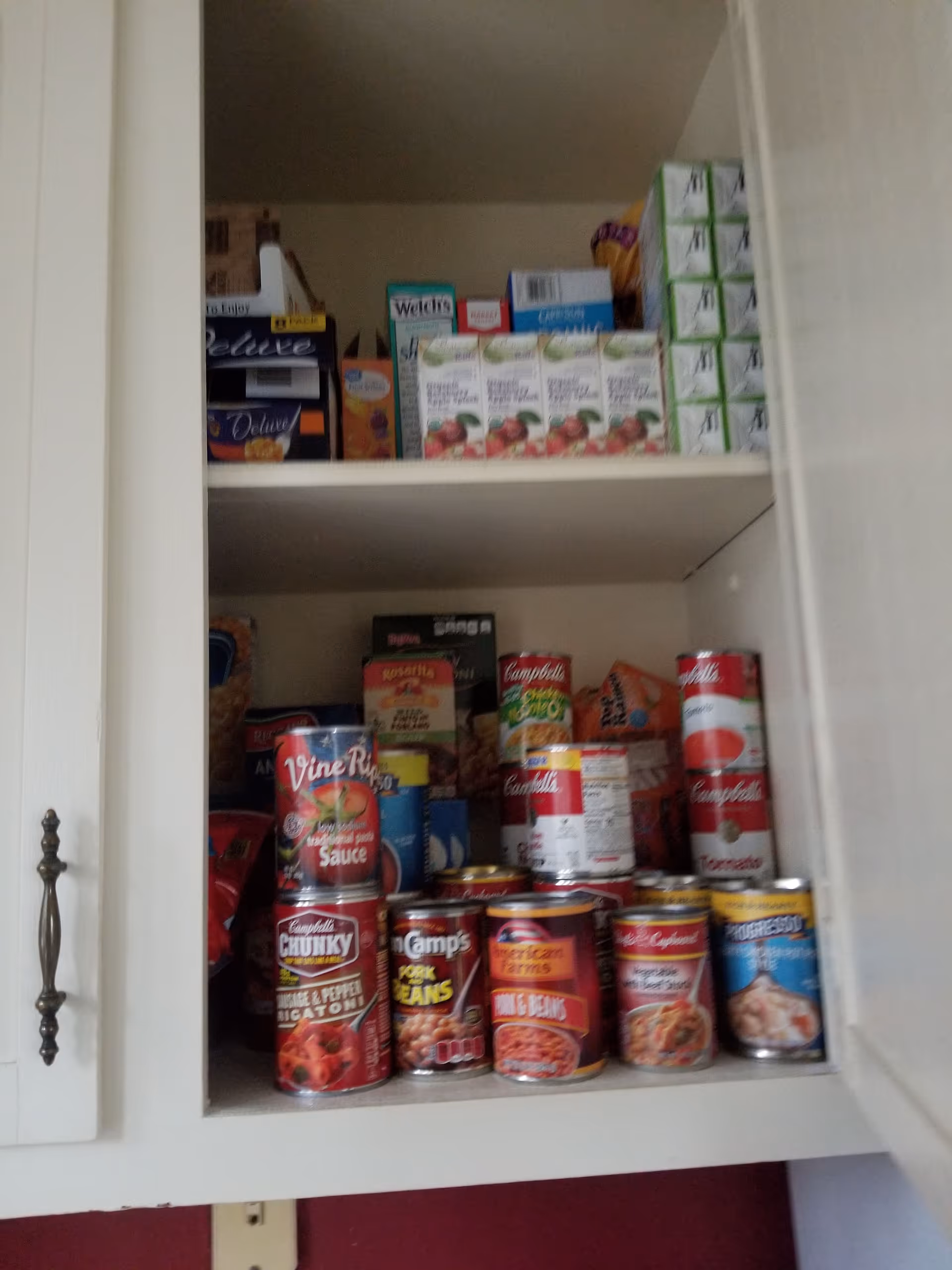 Open cabinet filled with canned soups, sauces, and boxed beverages on two shelves.