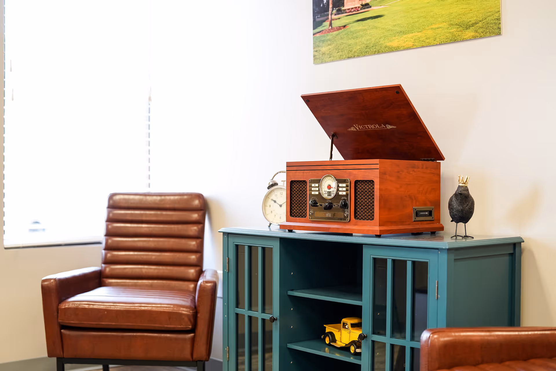 Brown leather armchair beside a teal cabinet with a vintage radio in a bright lounge.