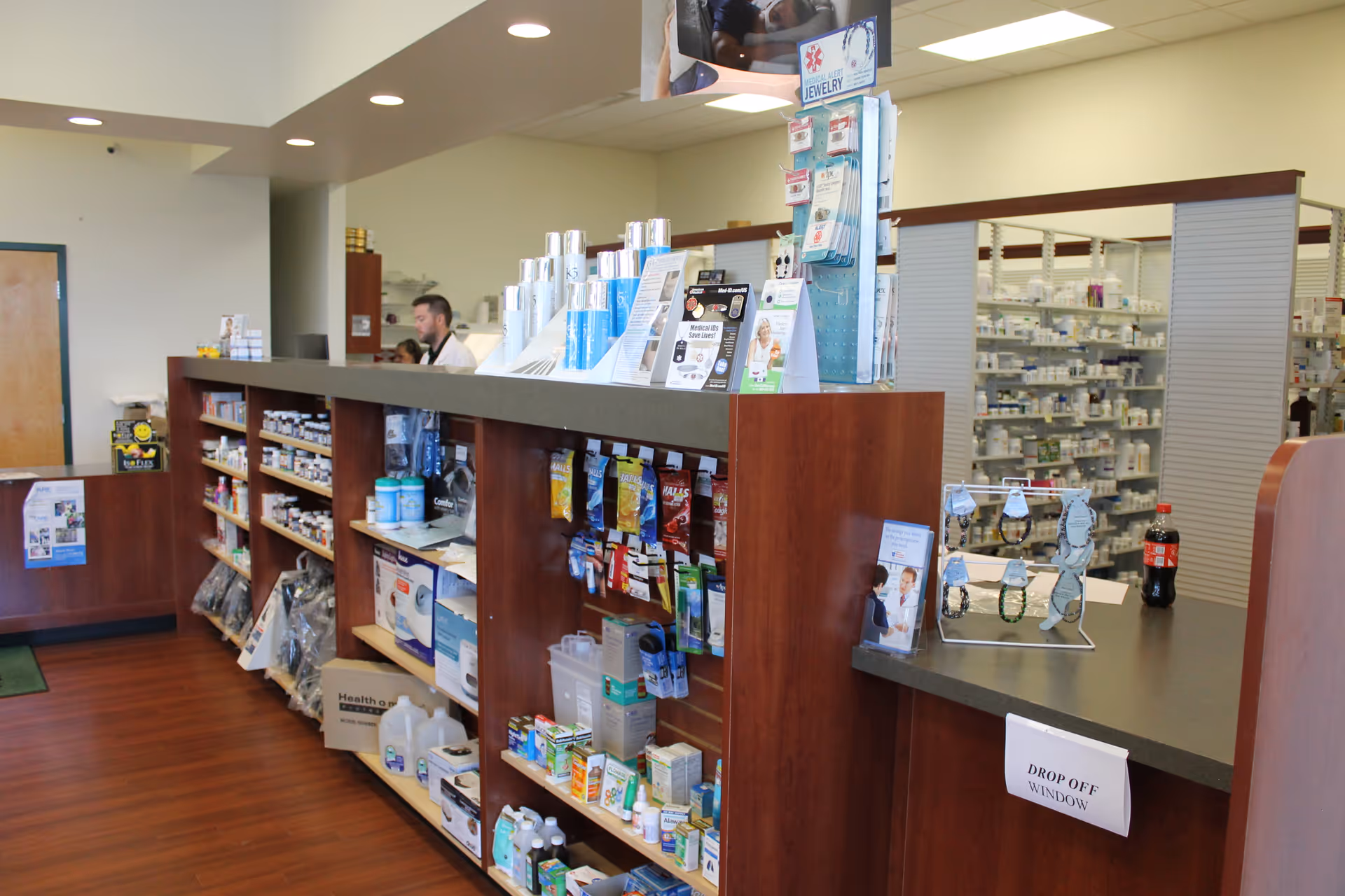 Interior view of a pharmacy counter with wooden shelves and staff behind.