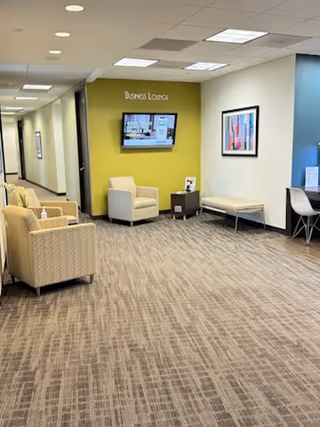 A modern indoor lounge area with beige chairs, a wall-mounted TV, and lime accent wall.