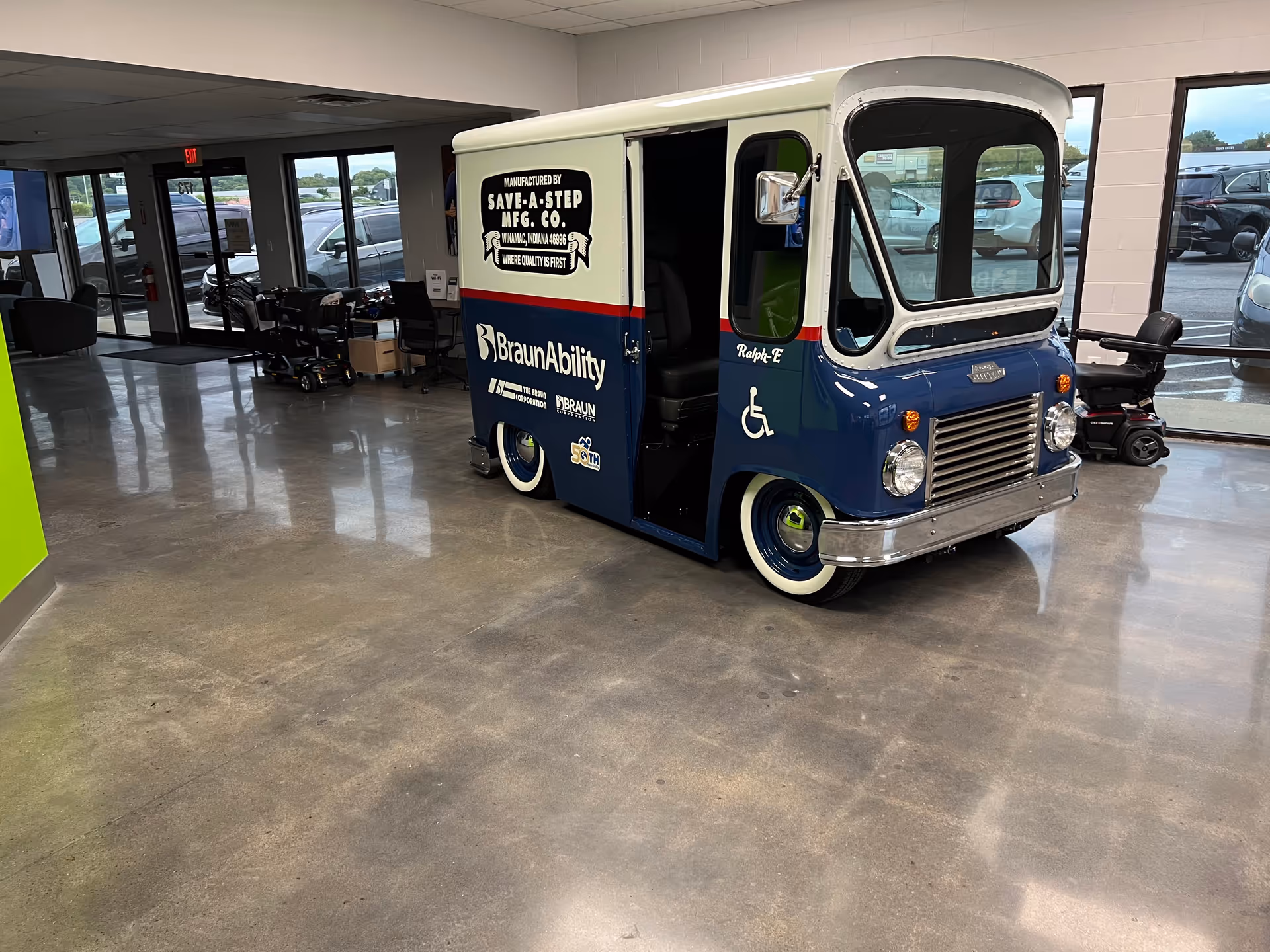 Blue and white mobility bus inside MobilityWorks showroom with seating and large windows.