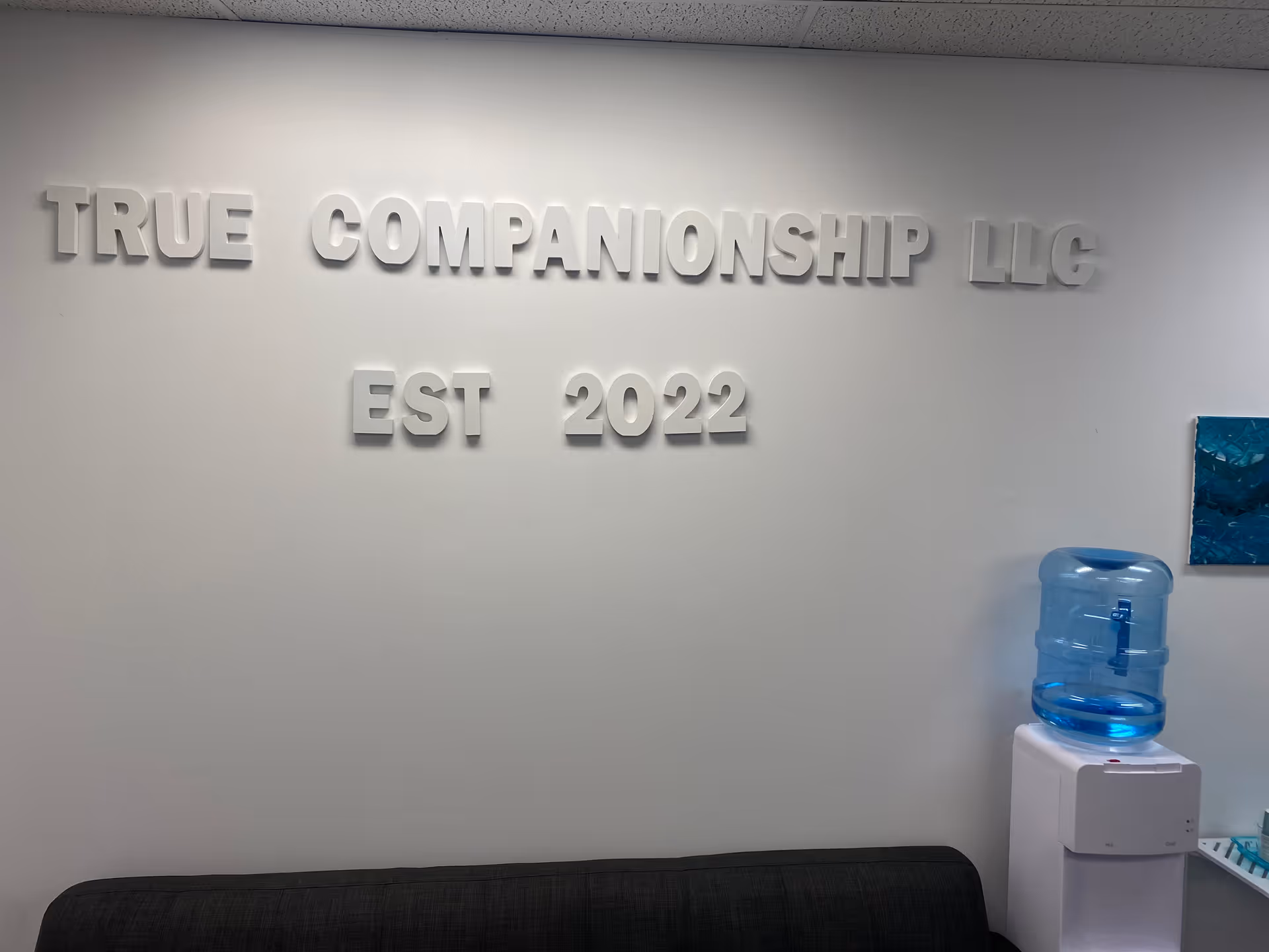 Interior lobby area with large True Companionship LLC sign and water cooler.