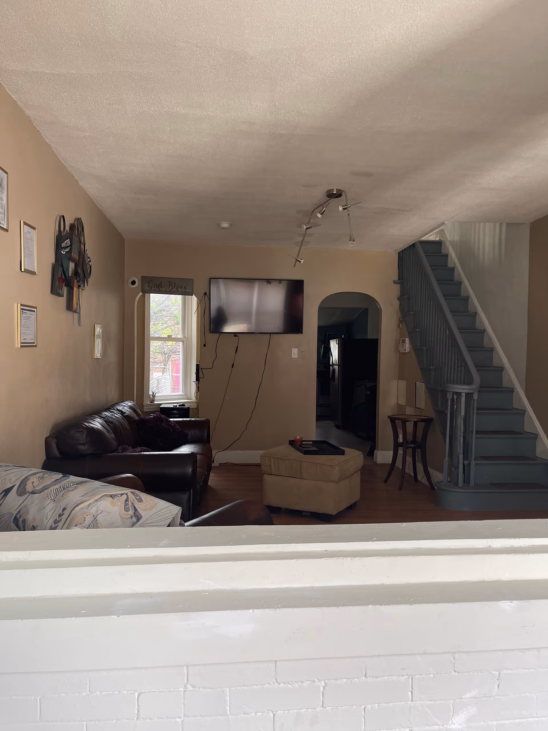 Cozy living room with leather sofa, ottoman, wall TV, window, and staircase.