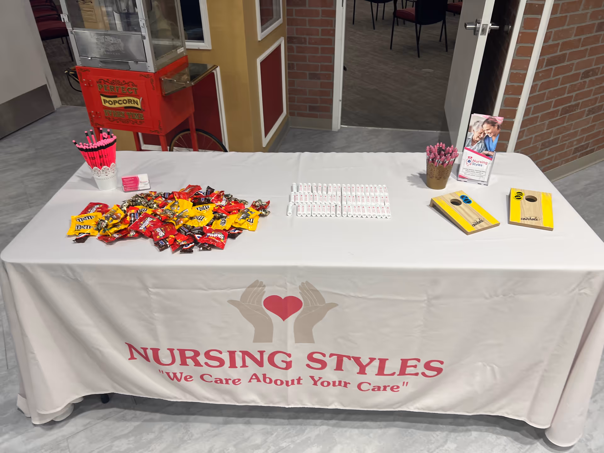 A table covered with Nursing Styles branding displays candy, pens, and brochures in a lobby.