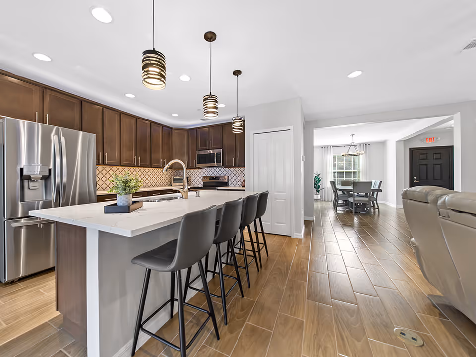 Modern kitchen with island, bar stools, stainless refrigerator, and connected dining area.