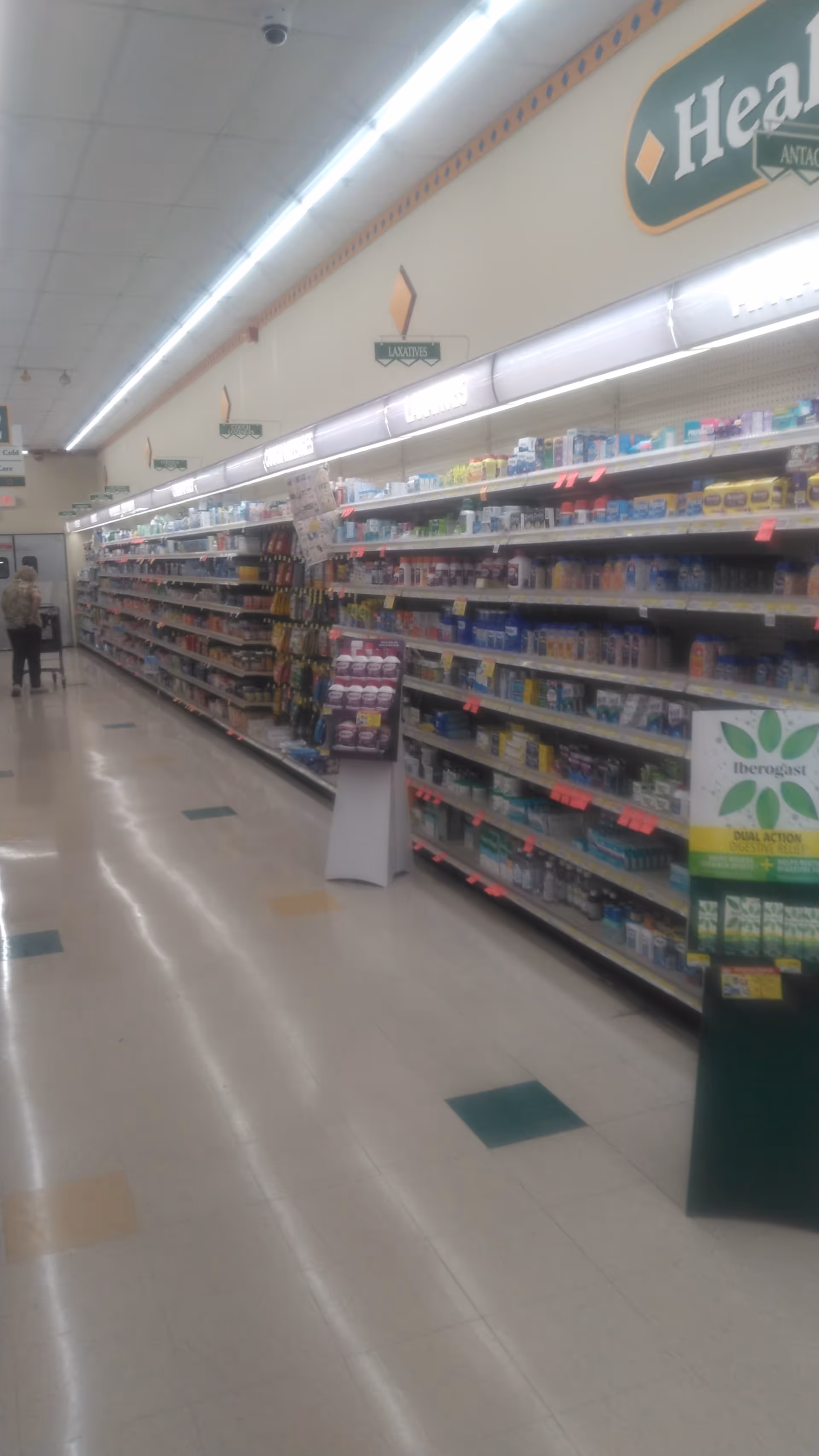 Long pharmacy aisle with shelves stocked with medications and health products.