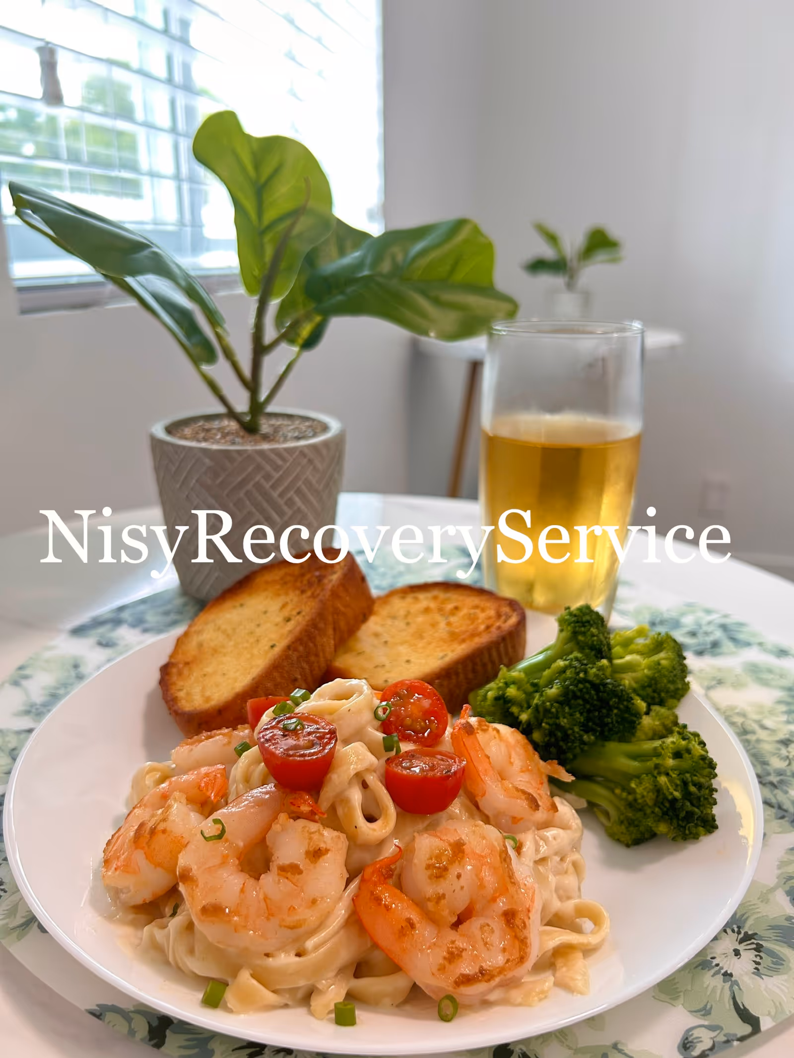 Plate of shrimp pasta with broccoli and bread on a dining table, beer glass nearby.