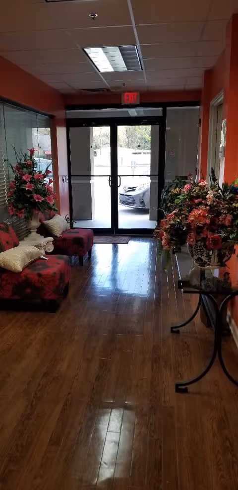 Interior lobby of a senior living facility featuring red walls, floral arrangements, and seating.