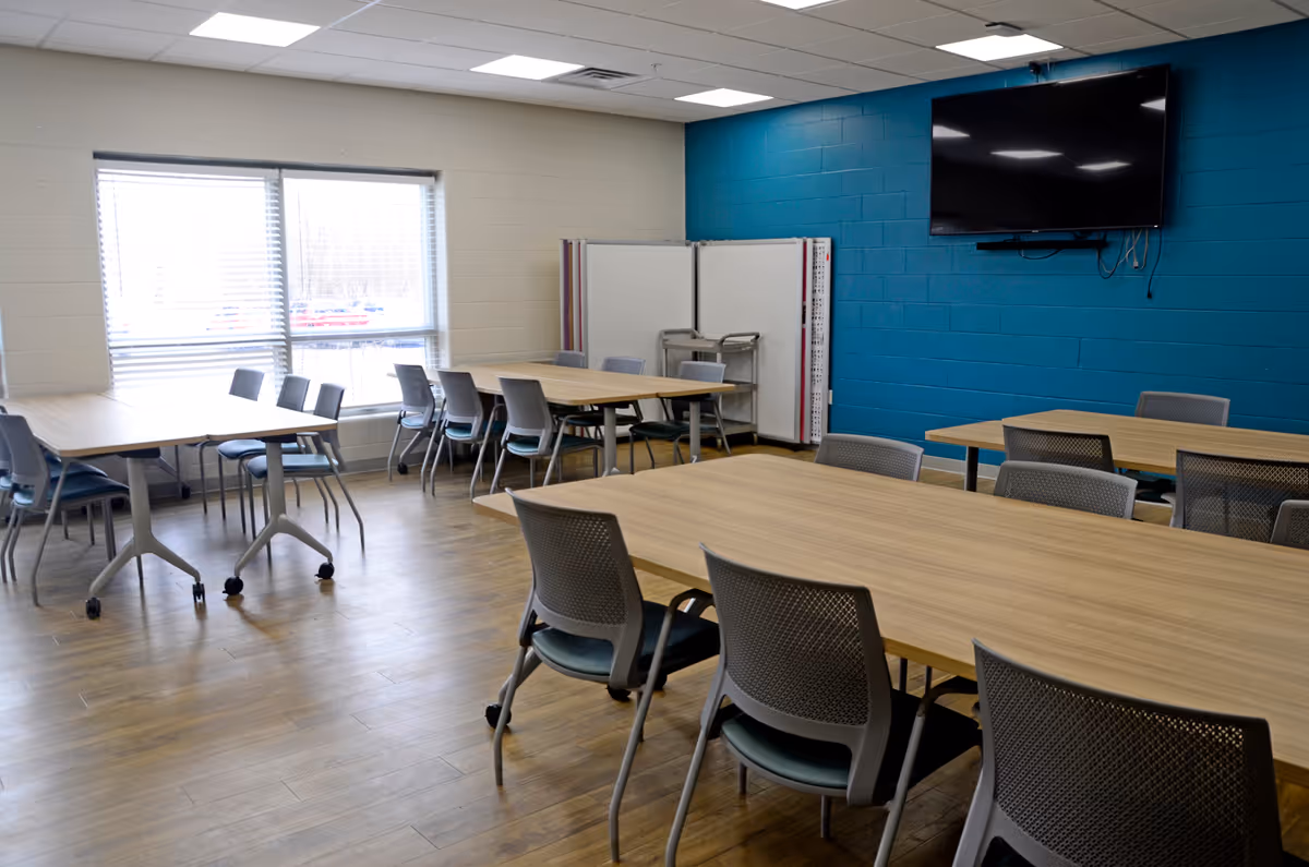 Bright, modern dining room with wooden tables, chairs, and a wall-mounted TV.
