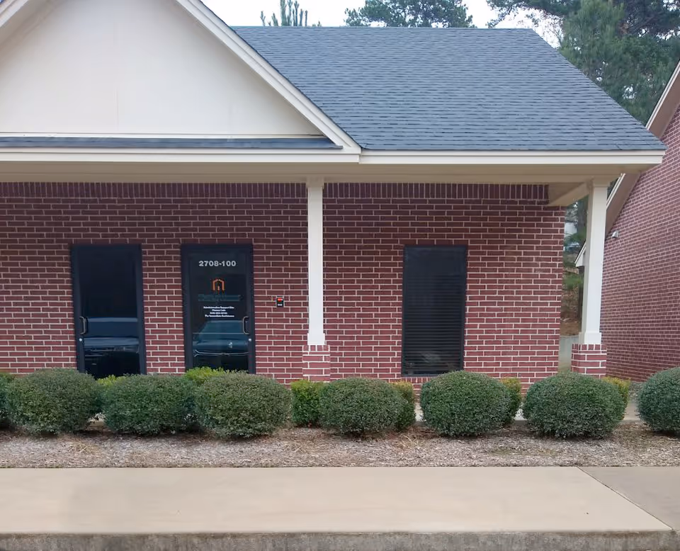 Brick senior living facility exterior with two dark doors, white columns, and trimmed hedges.