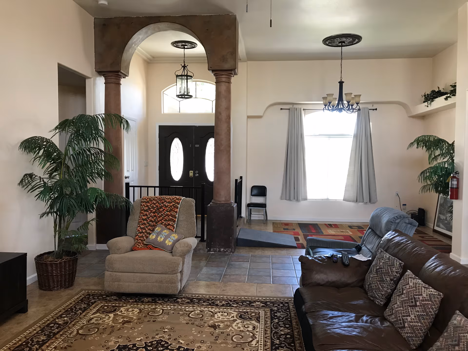 Spacious living room with arched doorway, columns, window light, couches, chairs, and potted plants.