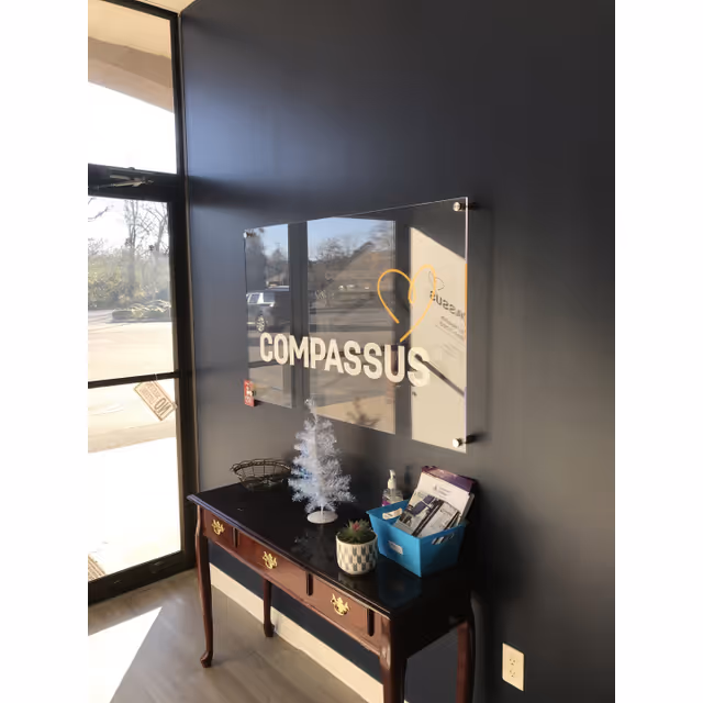 Interior lobby area with a Compassus sign mounted on a dark wall above a wooden console.