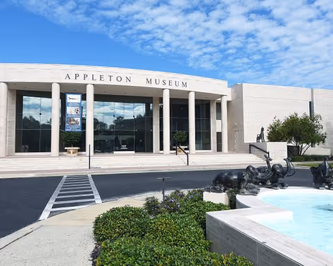 Appleton Museum exterior with glass entrance, columns, statues, and a surrounding fountain.