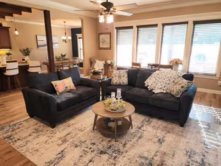 Cozy living room with dark sofas, round coffee table, rug, and large windows
