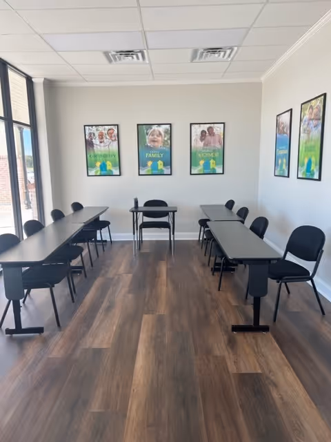 A bright conference room with long gray tables, black chairs, and wall art along back wall.