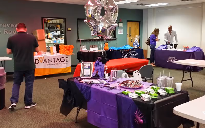 Indoor community fair setup with tables, balloons, and visitors at Emerald Senior Care.
