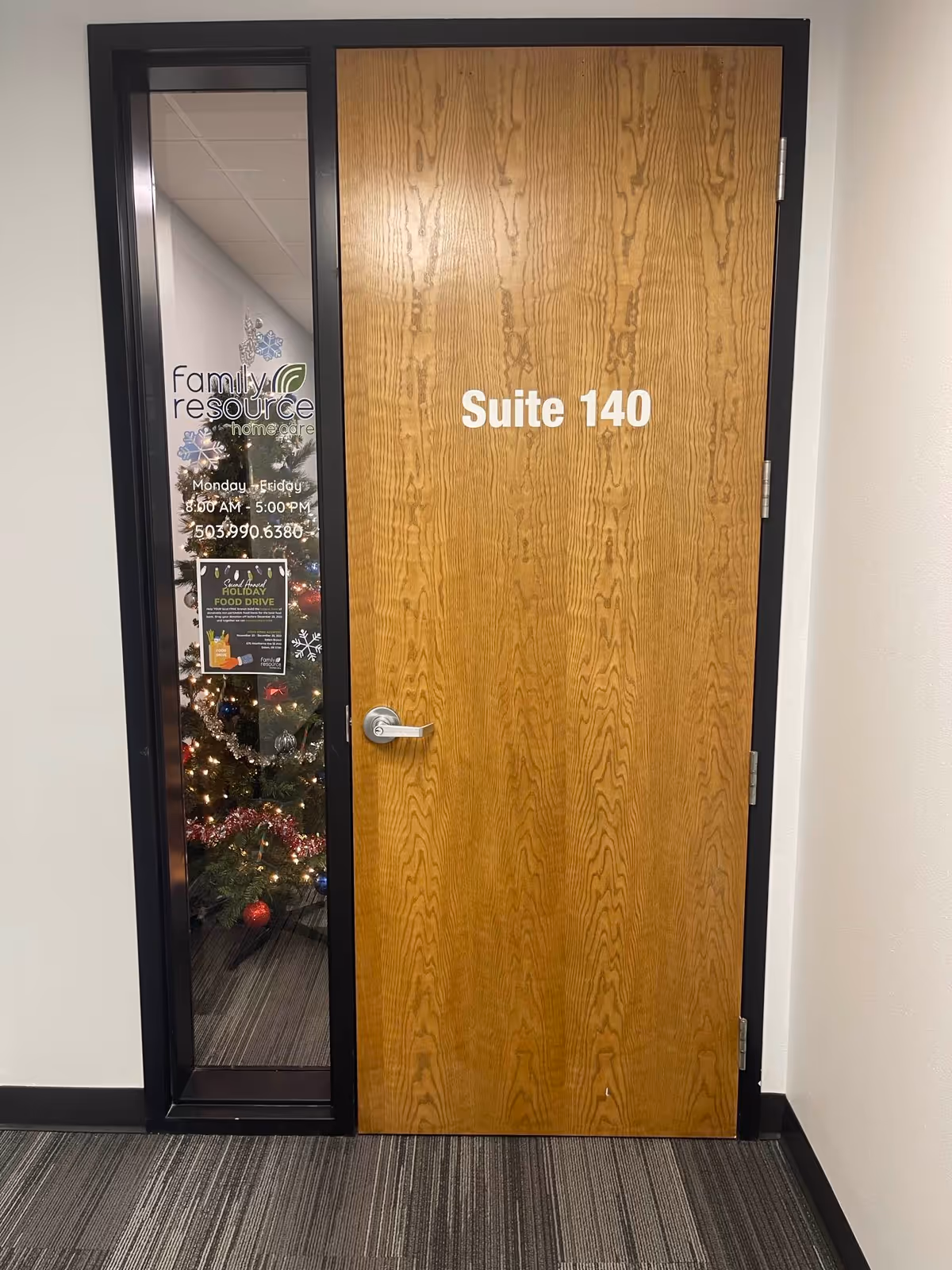 Wooden door labeled Suite 140 beside a glass panel with a holiday-decorated display.