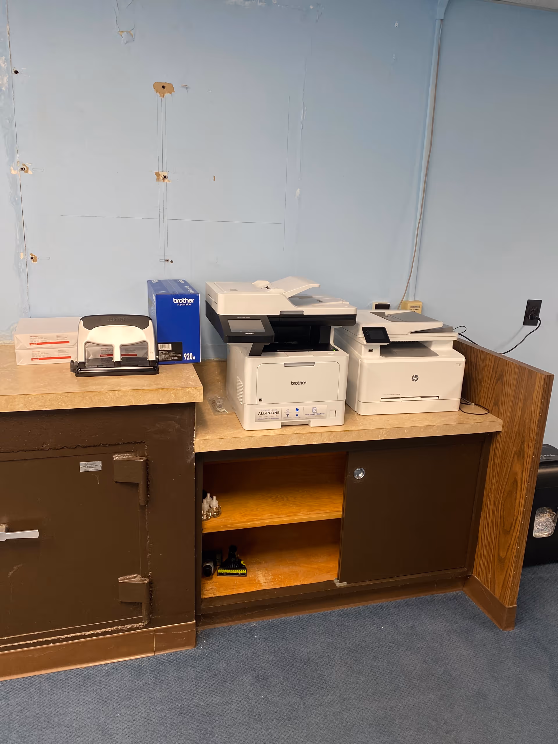Two printers on a wooden counter against a blue wall in a utility area.