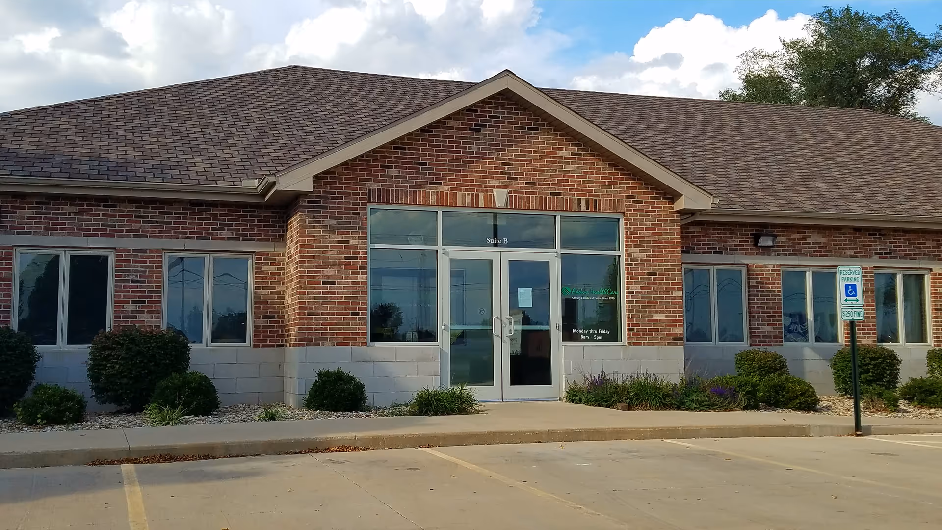 Brick senior living facility entrance with glass doors, landscaping, and a handicap parking sign.