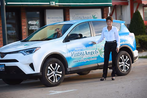 Visiting Angels SUV parked in front of a storefront, with a staff member standing beside it.
