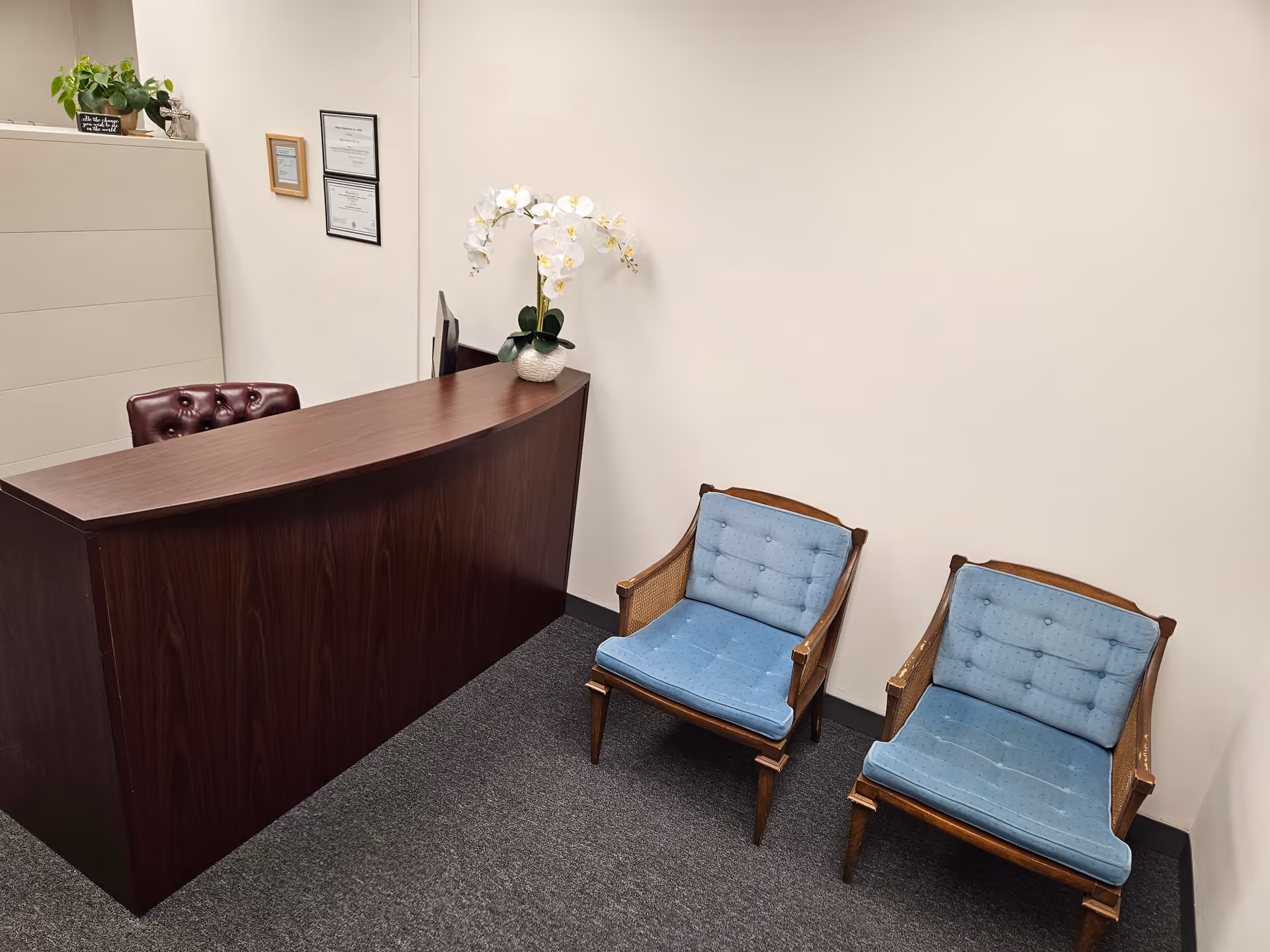 Reception desk with dark wood counter and two blue cushioned chairs in a small lobby.