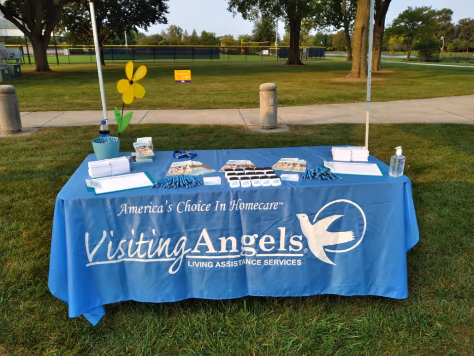 Outdoor table with a blue Visiting Angels banner and promotional materials in a park.
