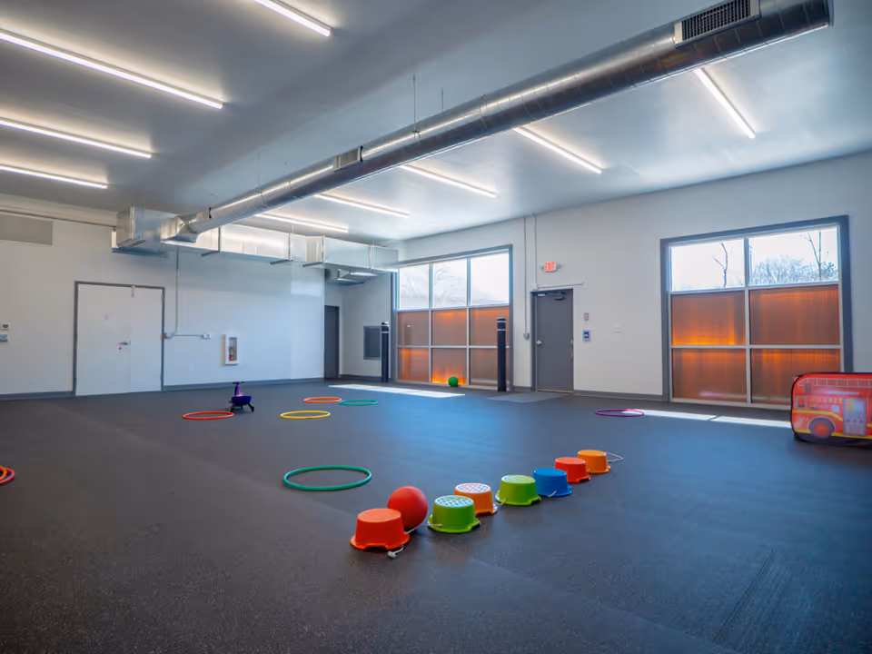 Large empty indoor activity room with colorful hoops, stools, and dark flooring.