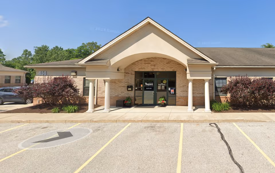 Front entrance of a Senior Helpers facility with arches and columns, parking lot in foreground.
