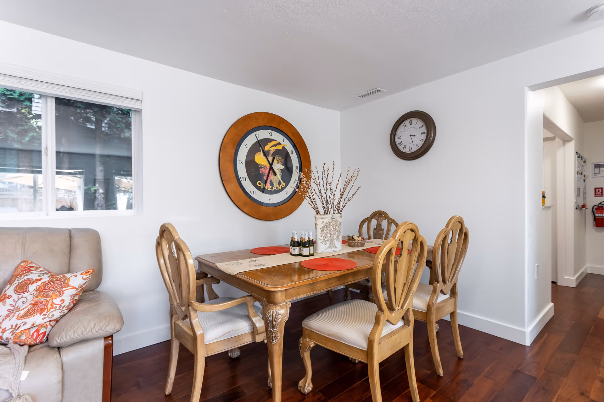 Cozy dining room with wooden table, chairs, wall clock, and decorative centerpiece.