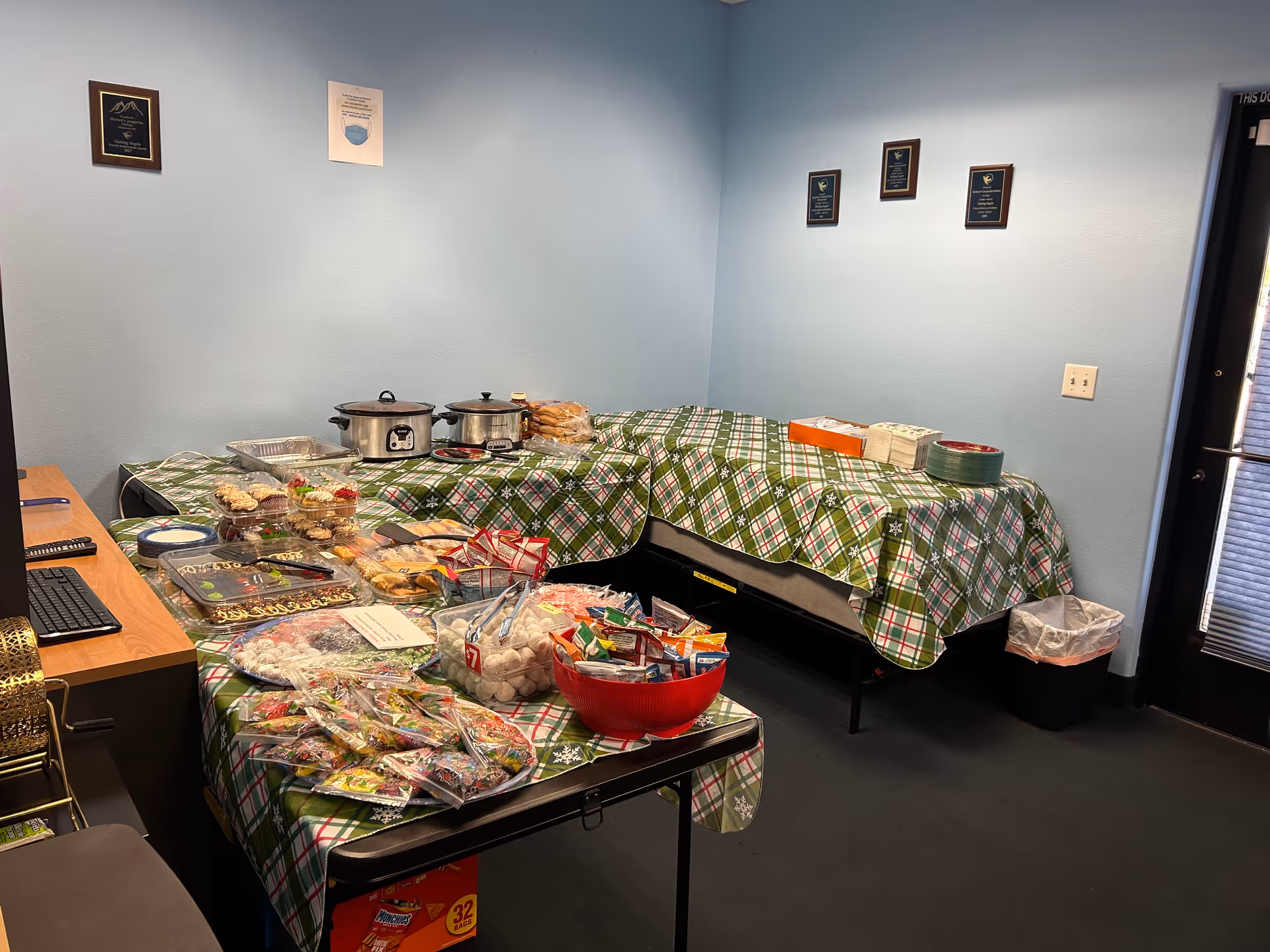 Tables covered with plaid cloths hold snacks, slow cookers, and food trays in a dining area.
