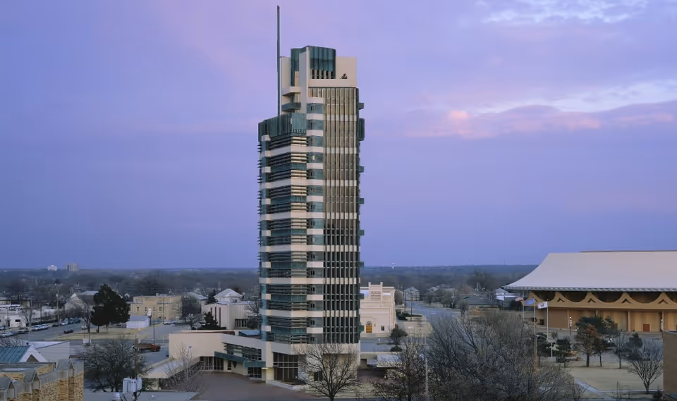 Tall modern tower surrounded by low buildings and a curved-roof structure