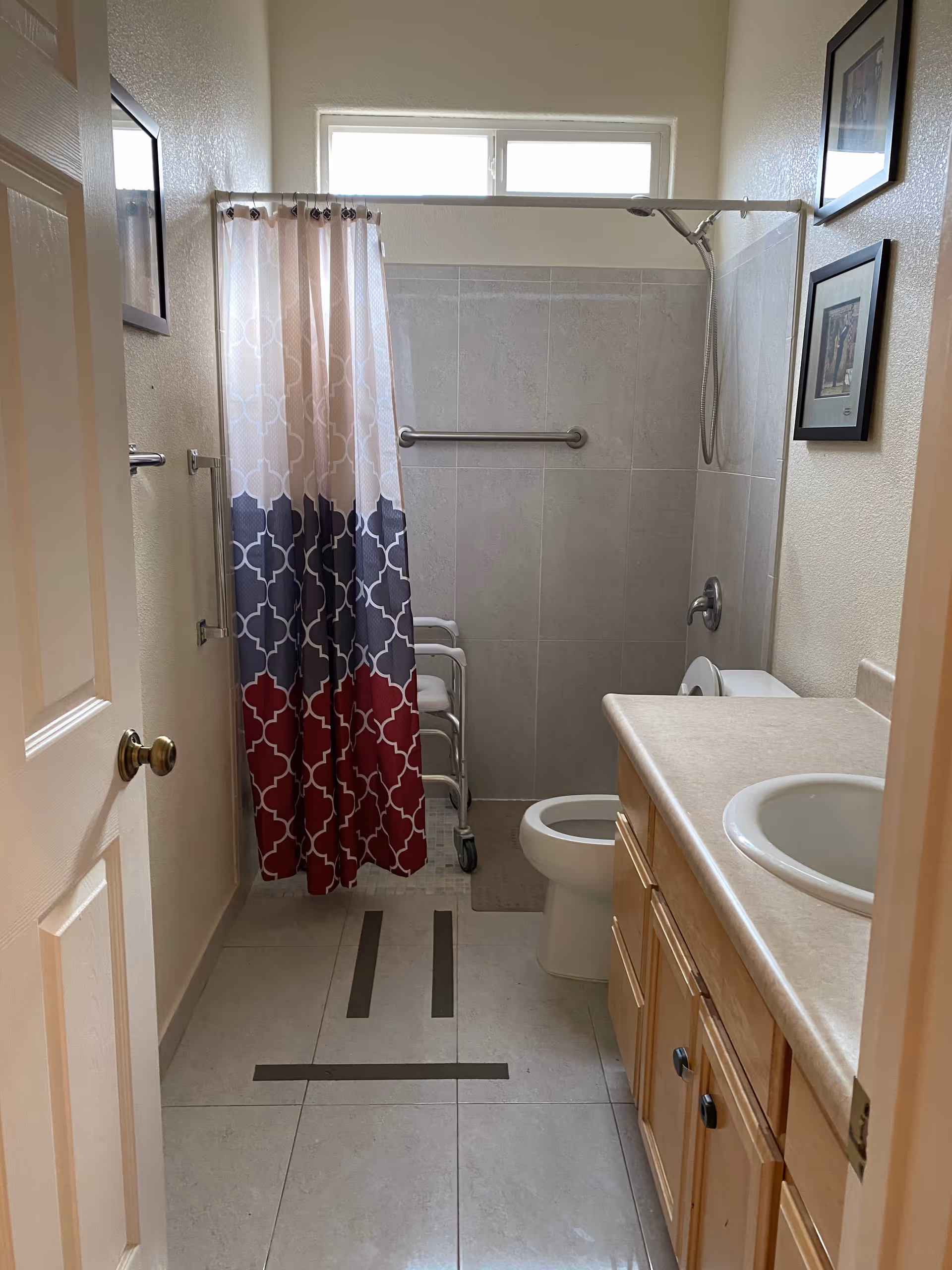 Senior living bathroom with a shower, patterned curtain, walker, toilet, and sink.