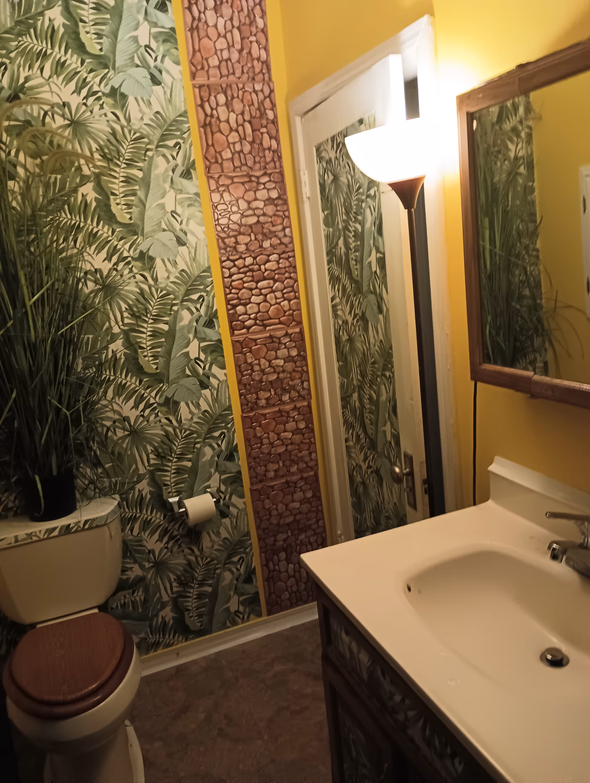 Tropical wallpaper bathroom with sink, toilet, mirror, and yellow walls.