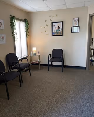 A small waiting area with chairs, a side table with a lamp, and wall art.