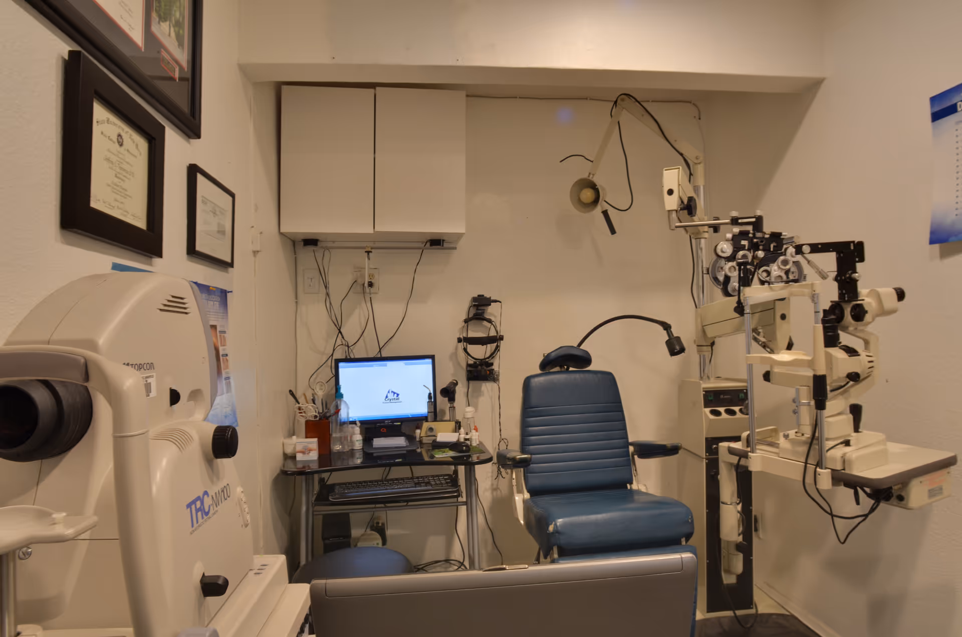 Eye exam room with blue chair, diagnostic equipment, computer, and white cabinets.