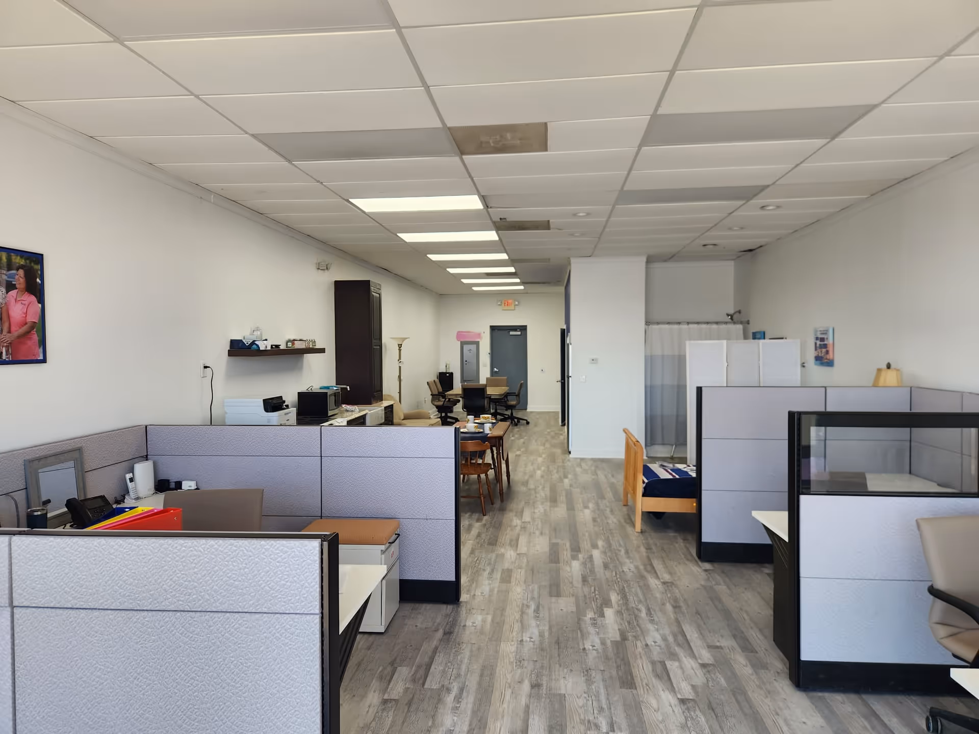 Open office-like common area with cubicles and desks; a bed is visible in the back.