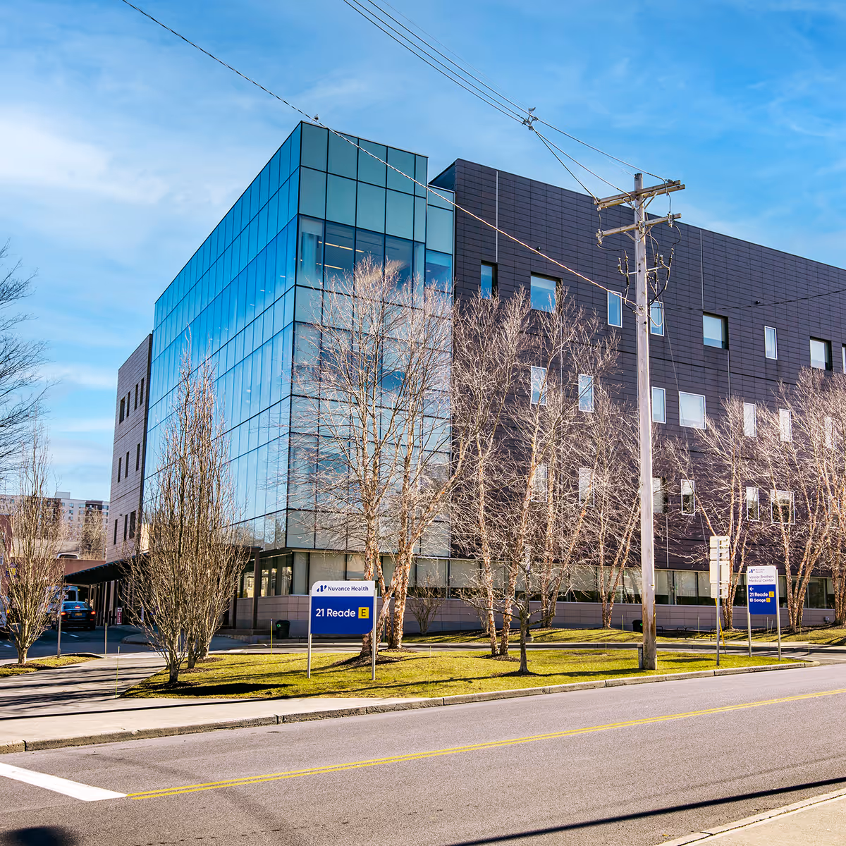 Modern medical office building with blue glass facade along a street and leafless trees.