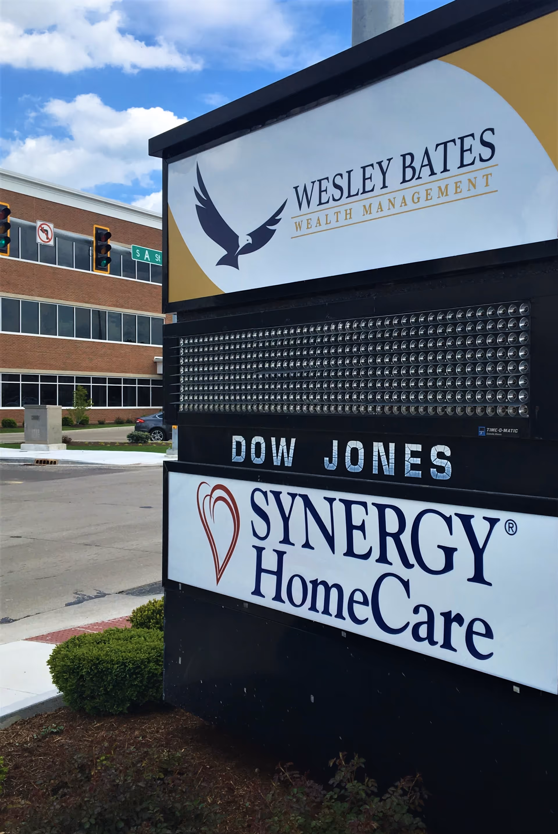 Exterior signboard displaying Dow Jones, Wesley Bates Wealth Management, and Synergy HomeCare branding.