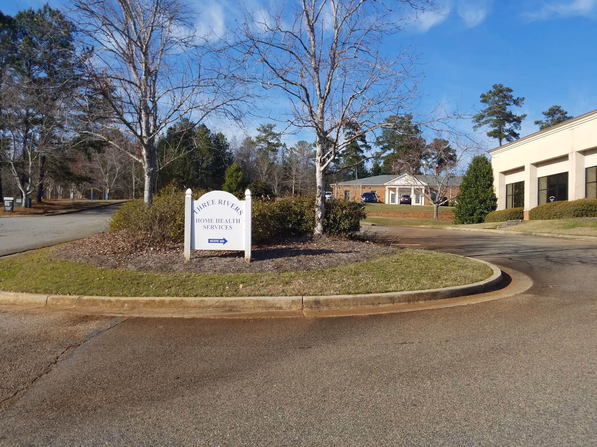 Circular driveway and landscaped island with a sign for Three Rivers Home Health Services, adjacent building.