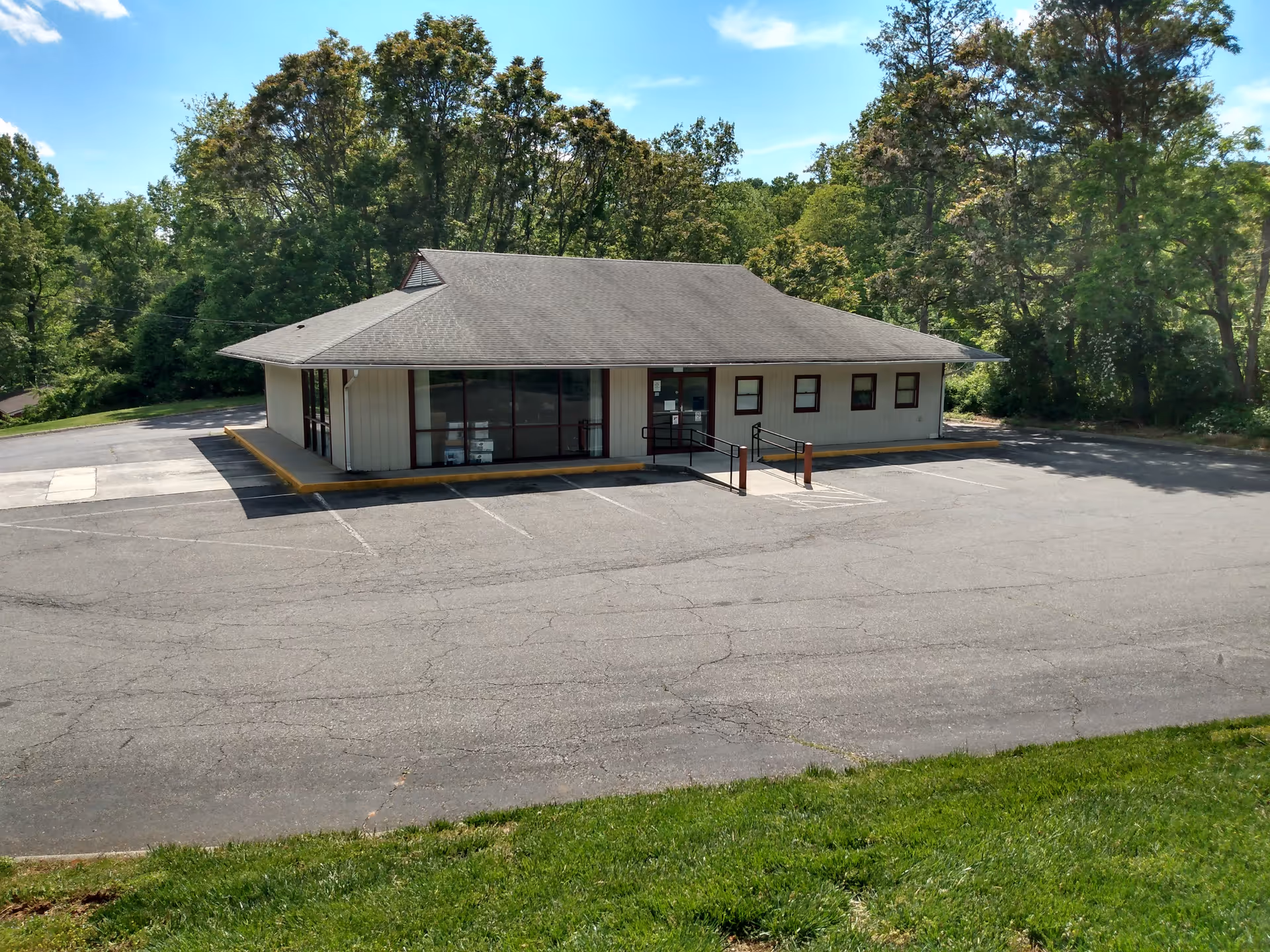 One-story beige building with glass front entrance, surrounded by trees and an empty parking lot.