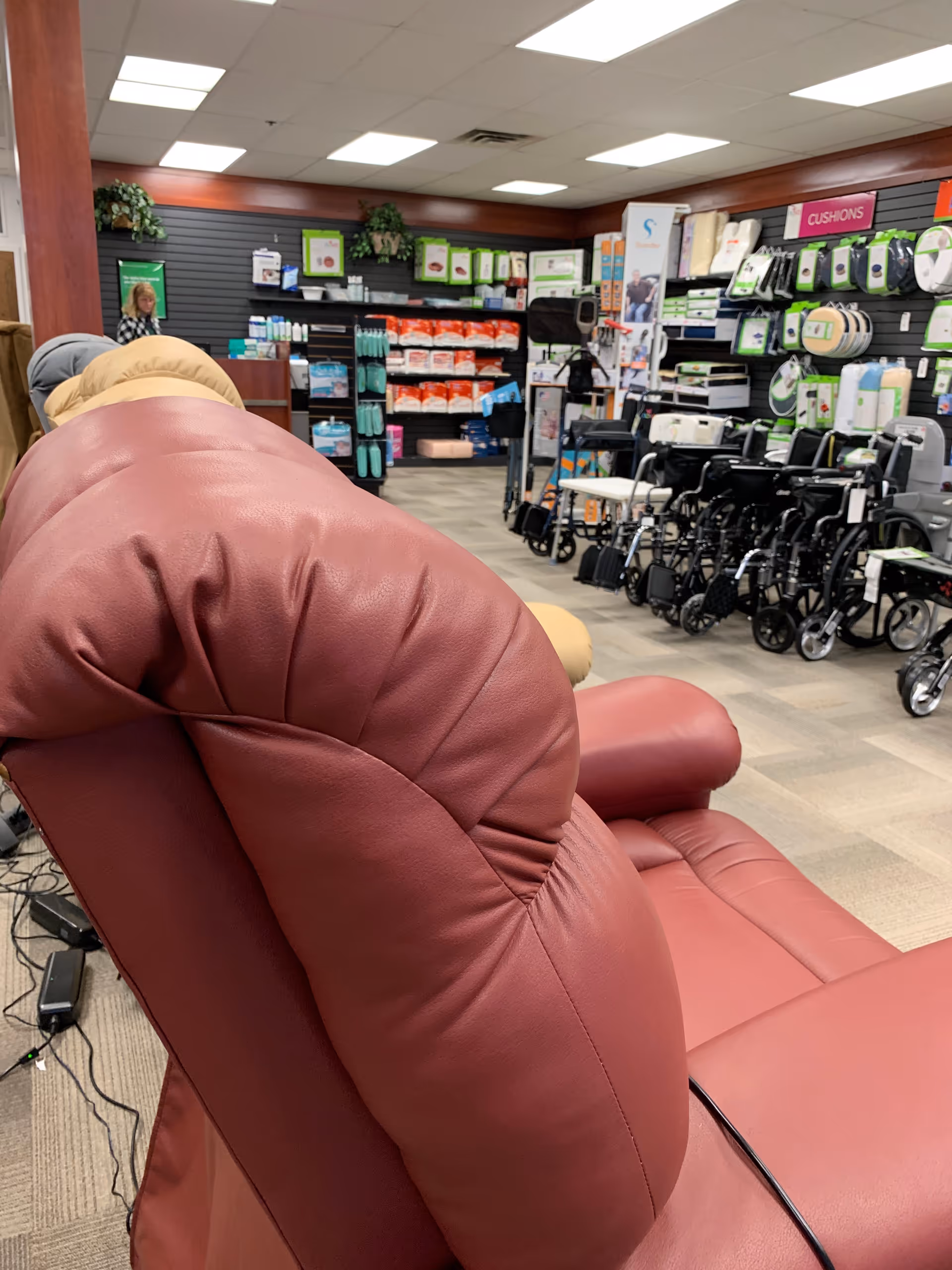 A red recliner chair in a medical supply store with wheelchairs and shelves.