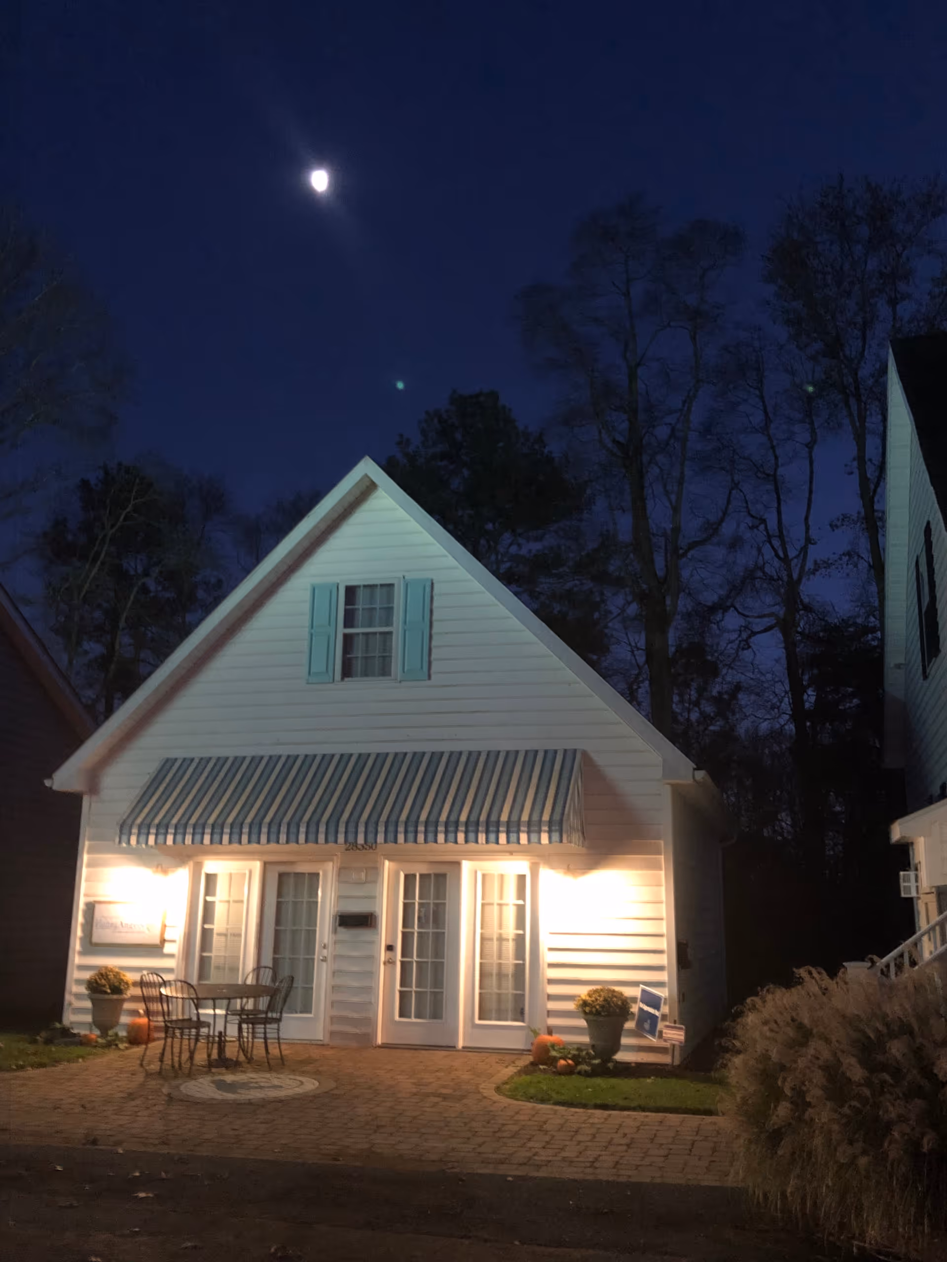 Night view of a white cottage-style building with striped awning and outdoor seating.