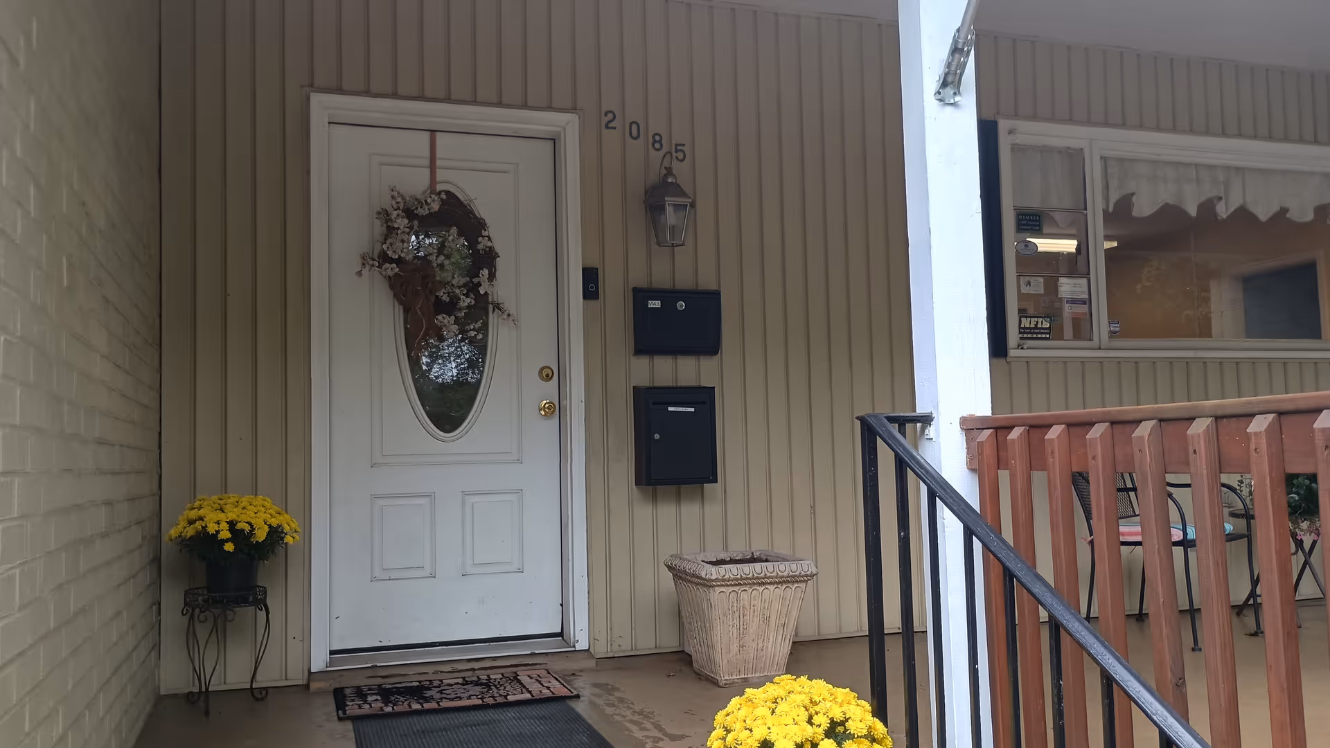 Front entrance of a Home Instead facility with wreath on door, yellow mums, mailboxes, and railing.