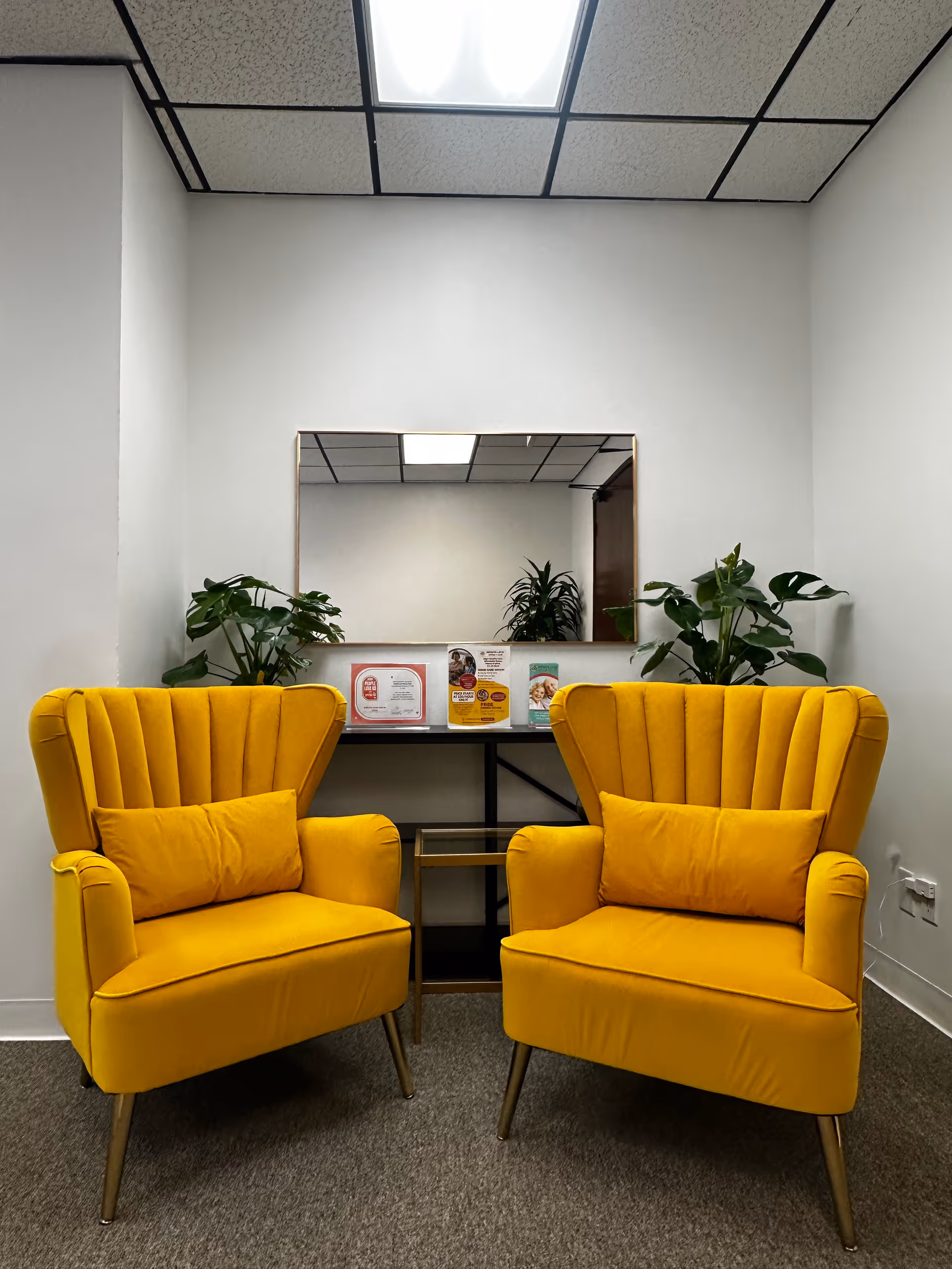 Two yellow upholstered armchairs flank a small table with brochures in a modern waiting area.