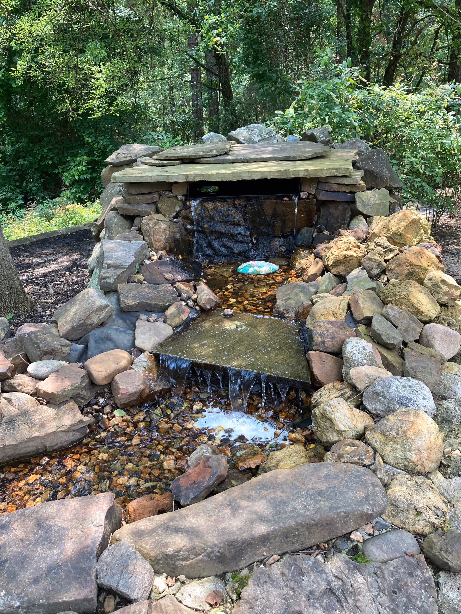 Rock waterfall feature built of stacked stones in a wooded outdoor garden.